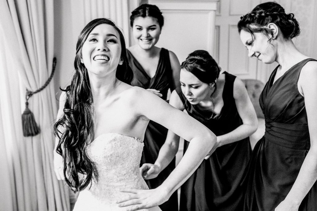 bridesmaids helping bride into dress