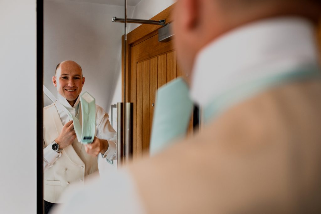 groom putting on a tie for wedding at great fosters