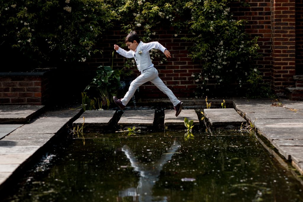 little boy jumping over pond at wedding