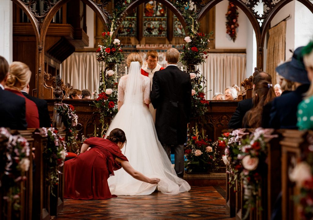 bridesmaid arranging brides dress in church aisle