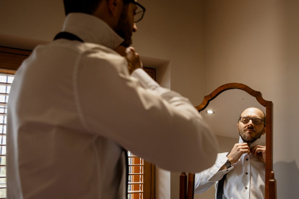 groom putting on tie in mirror