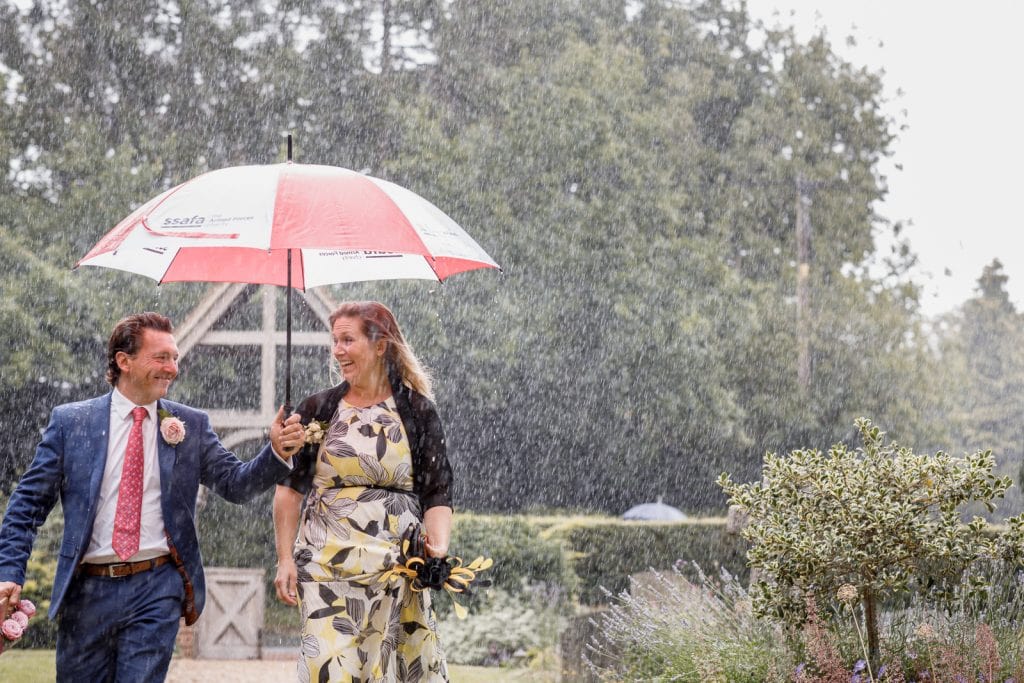 guests arriving to wedding in pouring rain with umbrella