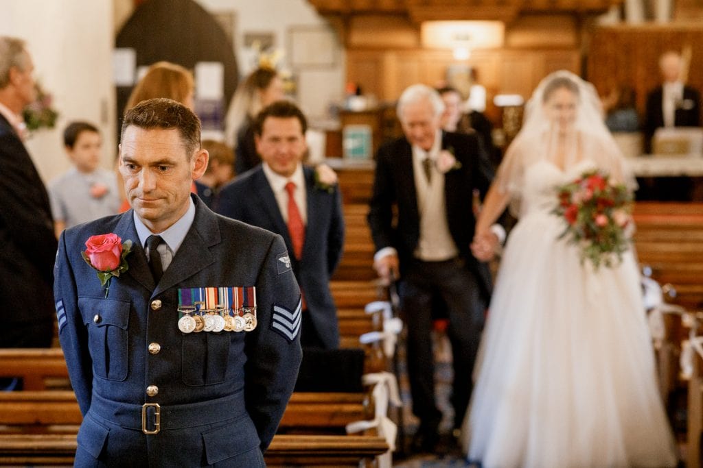 military groom waiting at front of church for bride arriving